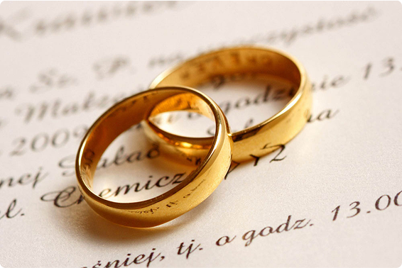 Two gold wedding rings are placed on top of a document with cursive writing, symbolizing marriage or commitment.